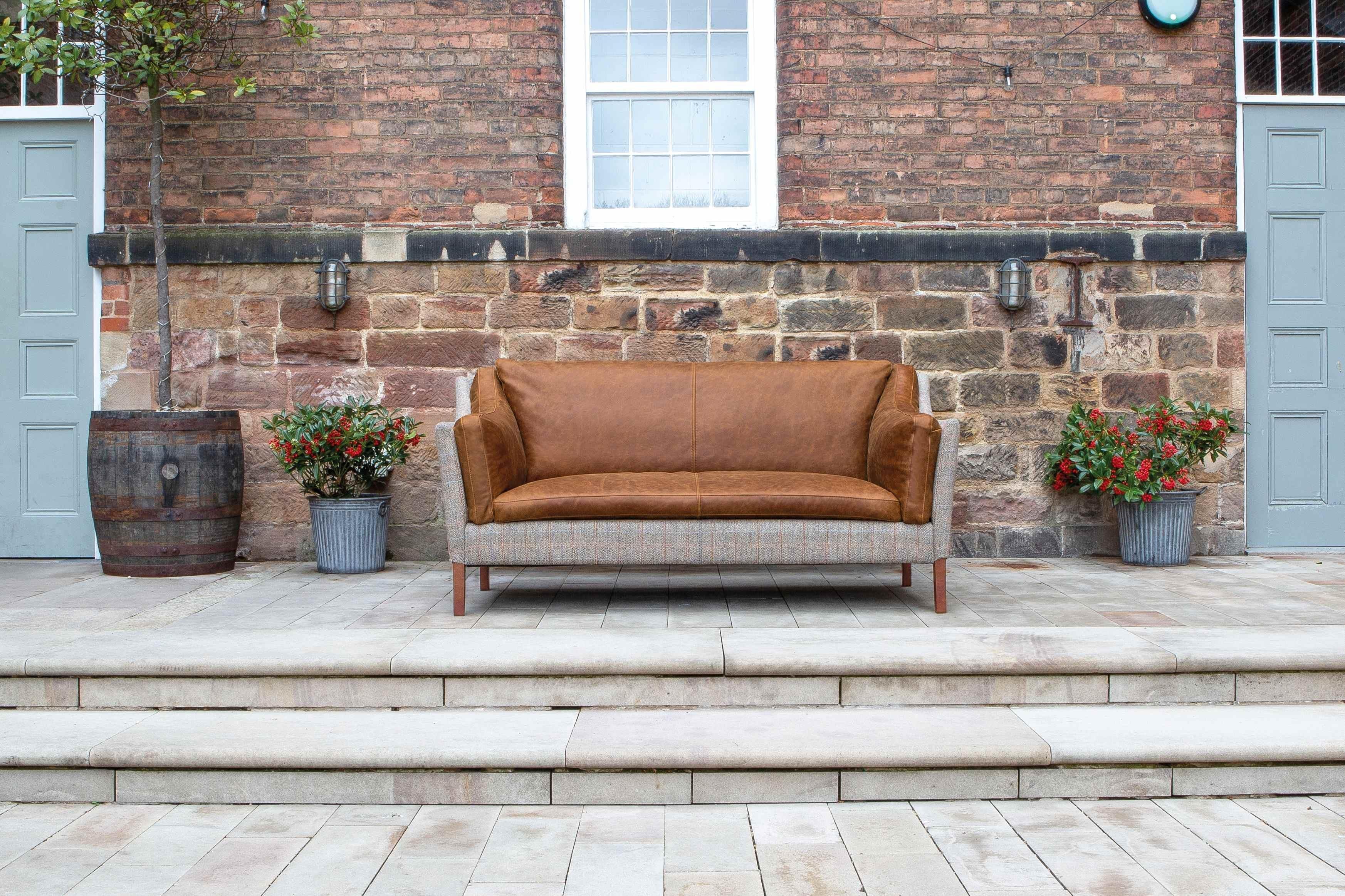Brown leather and fabric sofa on outdoor patio with stone steps and brick wall backdrop