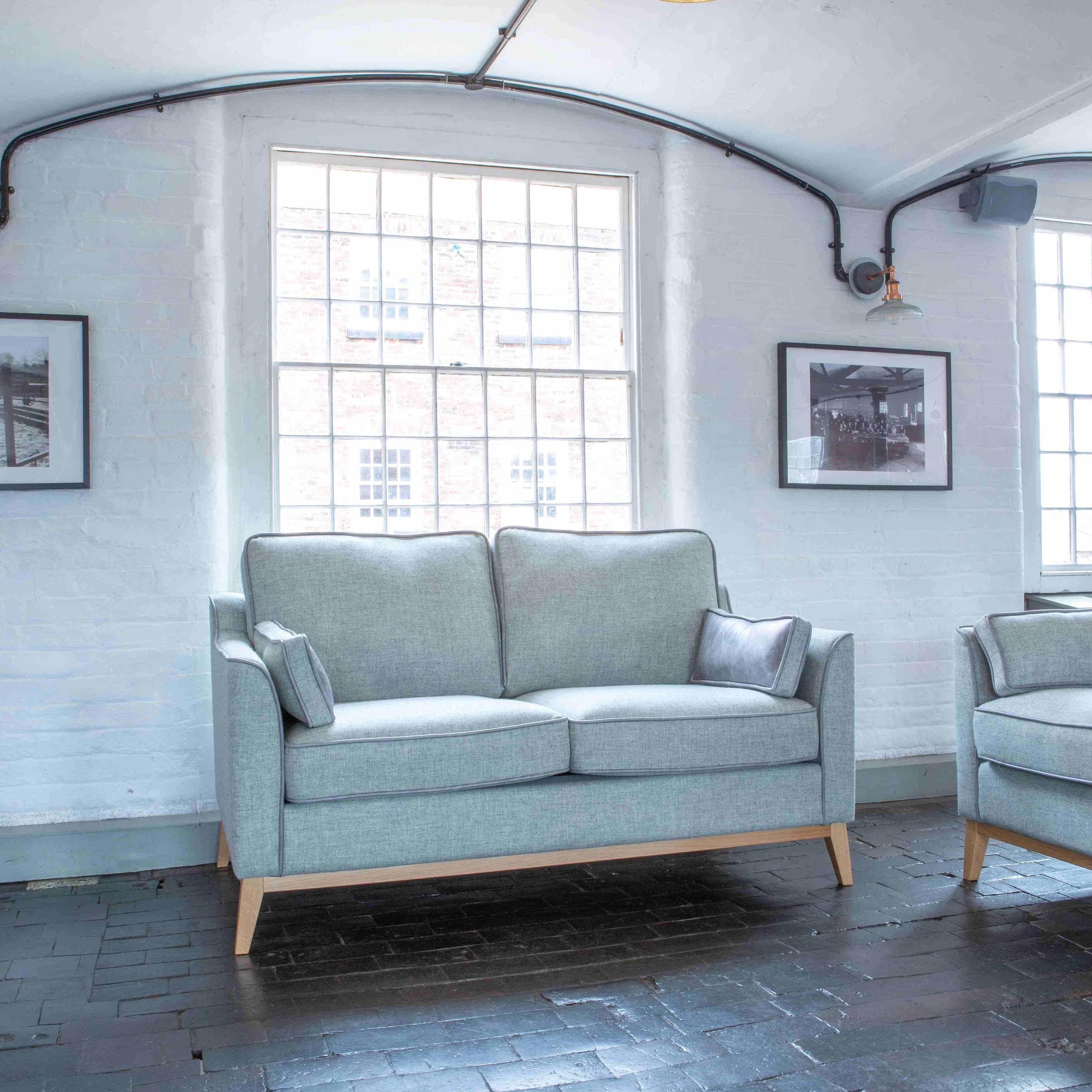 Light grey fabric sofa with wooden legs placed in a modern living room with large window