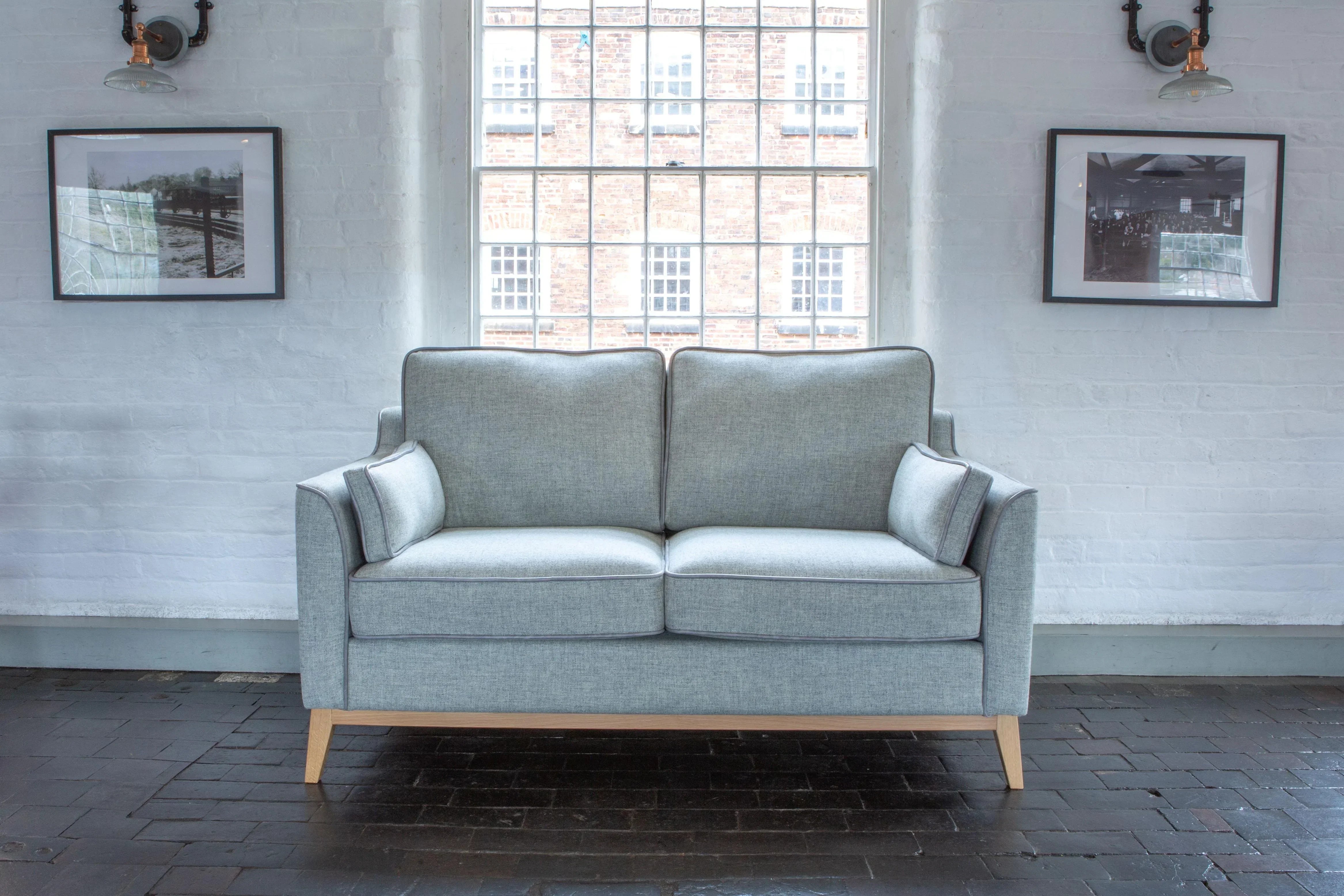 Light grey fabric sofa with wooden legs set against a window in a modern living room
