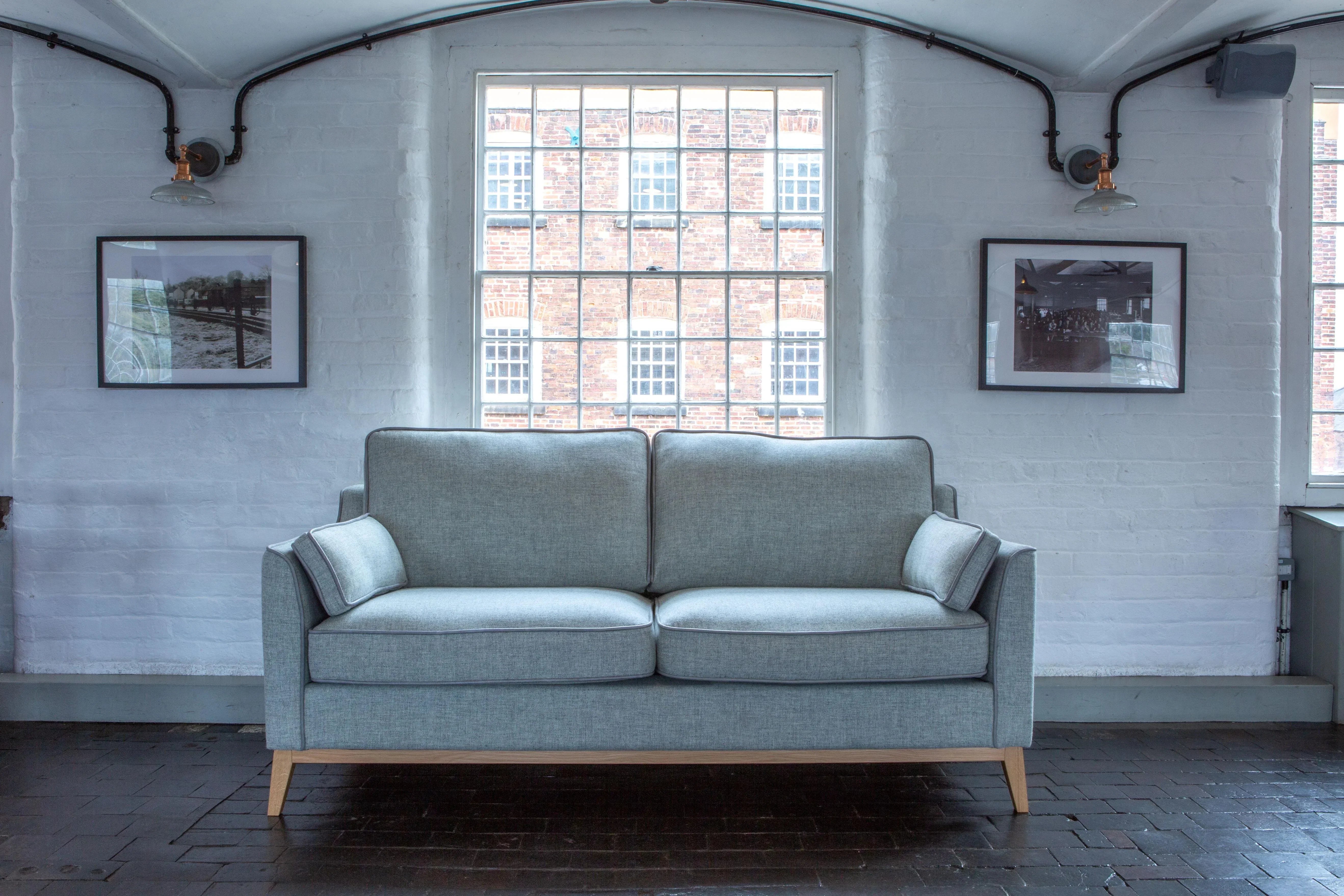 Light grey fabric sofa with wooden legs in modern living room with tall windows