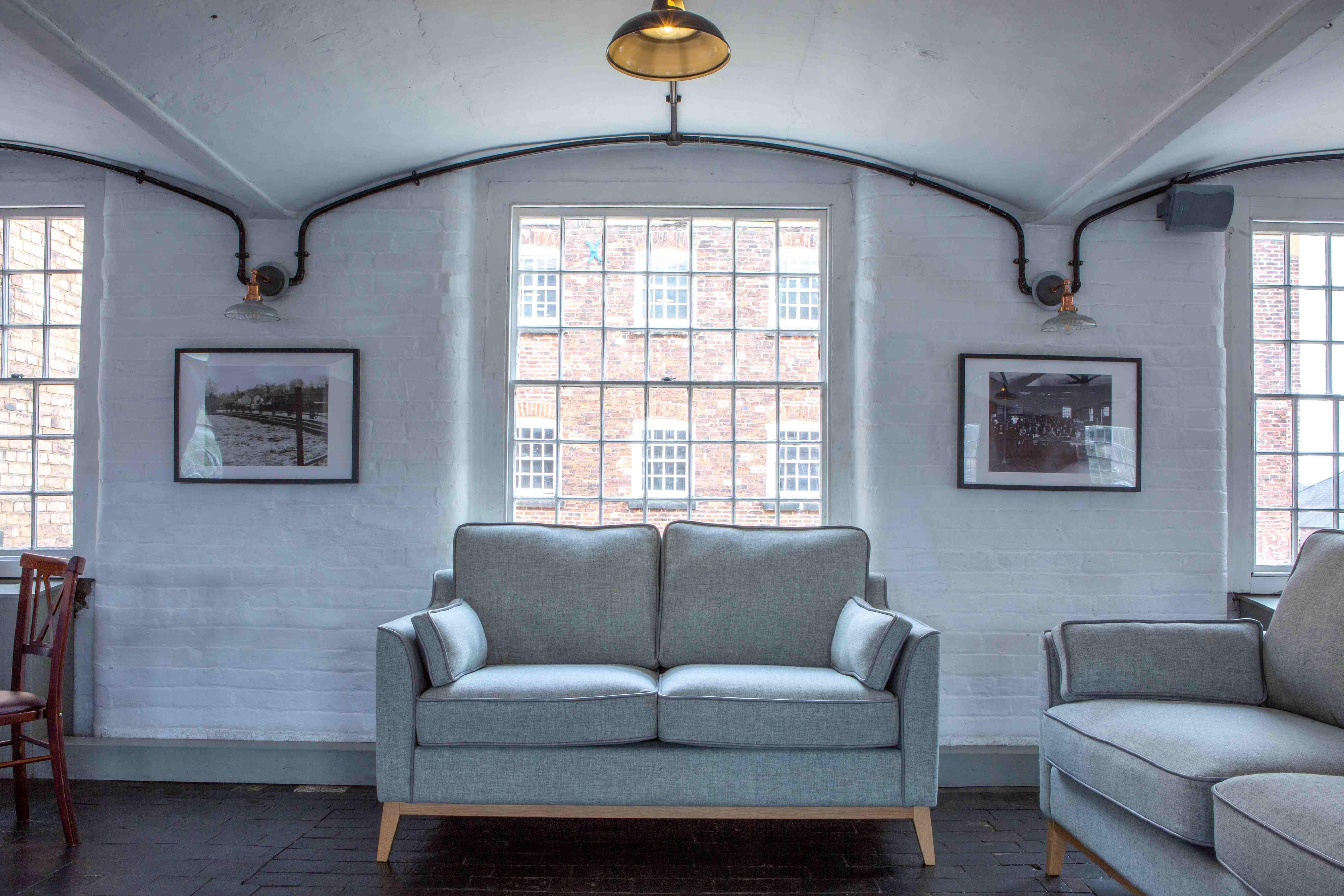 Light grey fabric sofa with wooden legs in a modern living room with large windows