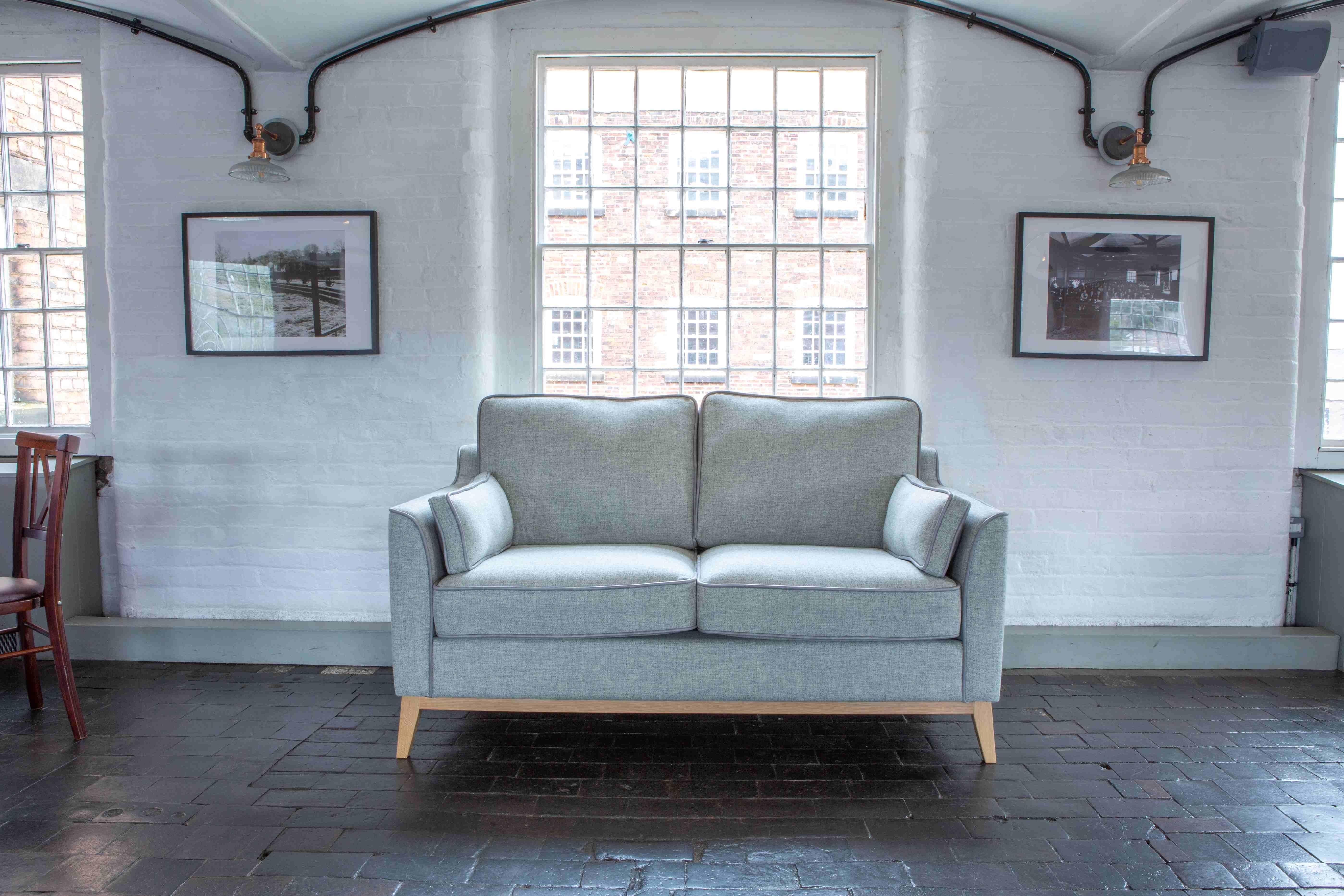 Light grey fabric sofa with wooden legs in modern living room with white brick walls
