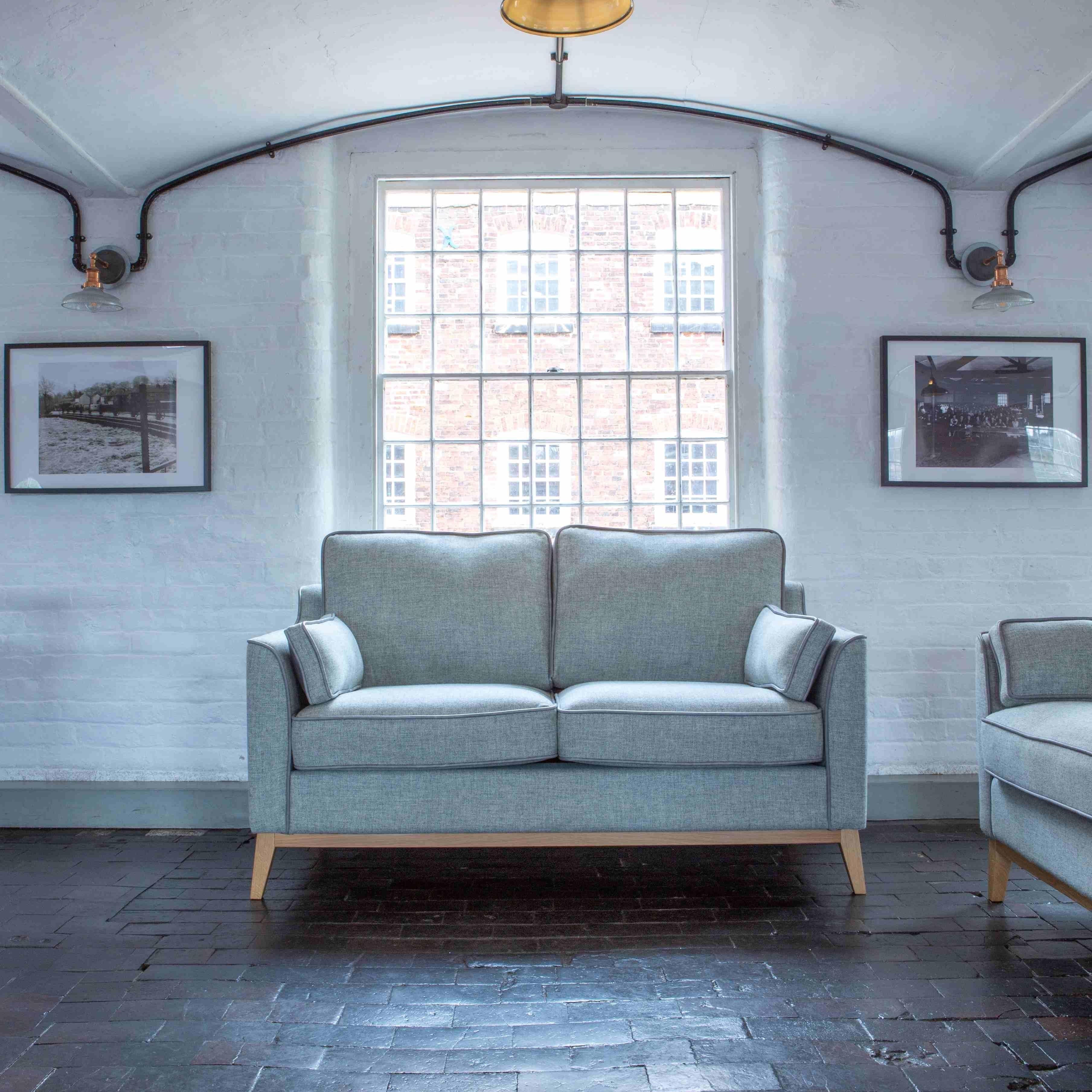Light grey fabric sofa with wooden legs in a bright living room with brick flooring