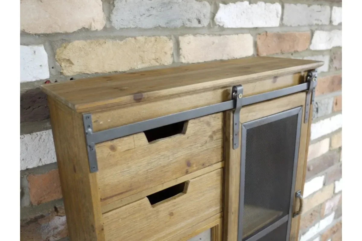 Rustic wooden cabinet with sliding metal door and two drawers against brick wall