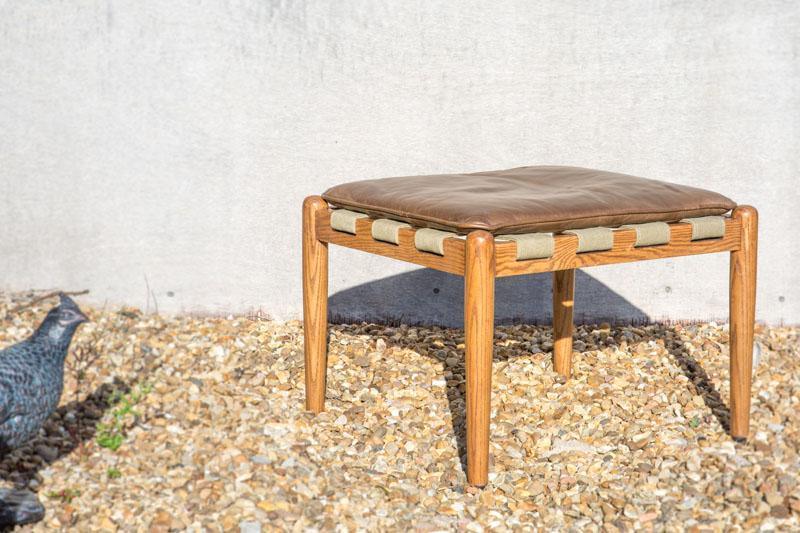 Wooden stool with brown leather cushion and woven detail on gravel patio