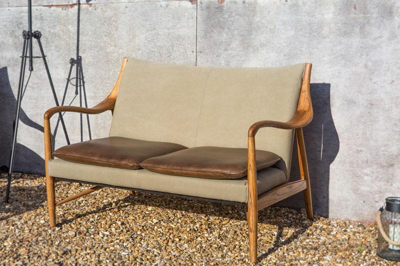 Outdoor wooden sofa with tan cushions and curved arms on gravel