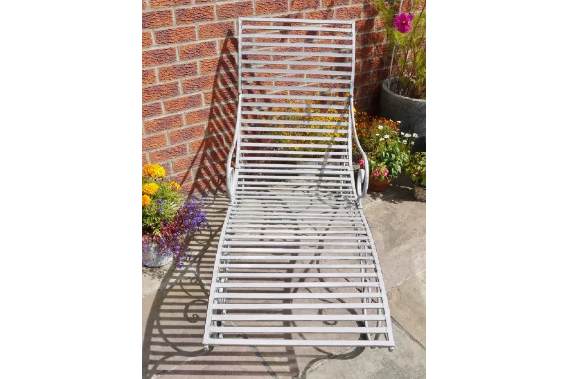 Metal garden lounger with slatted design on patio beside brick wall and potted flowers