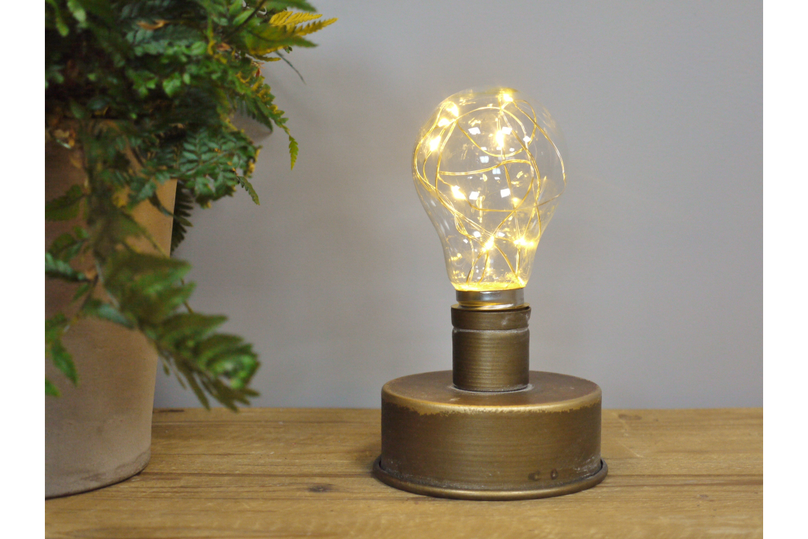 Small round industrial style metal light base with clear bulb containing warm white string lights, side view on wooden table.