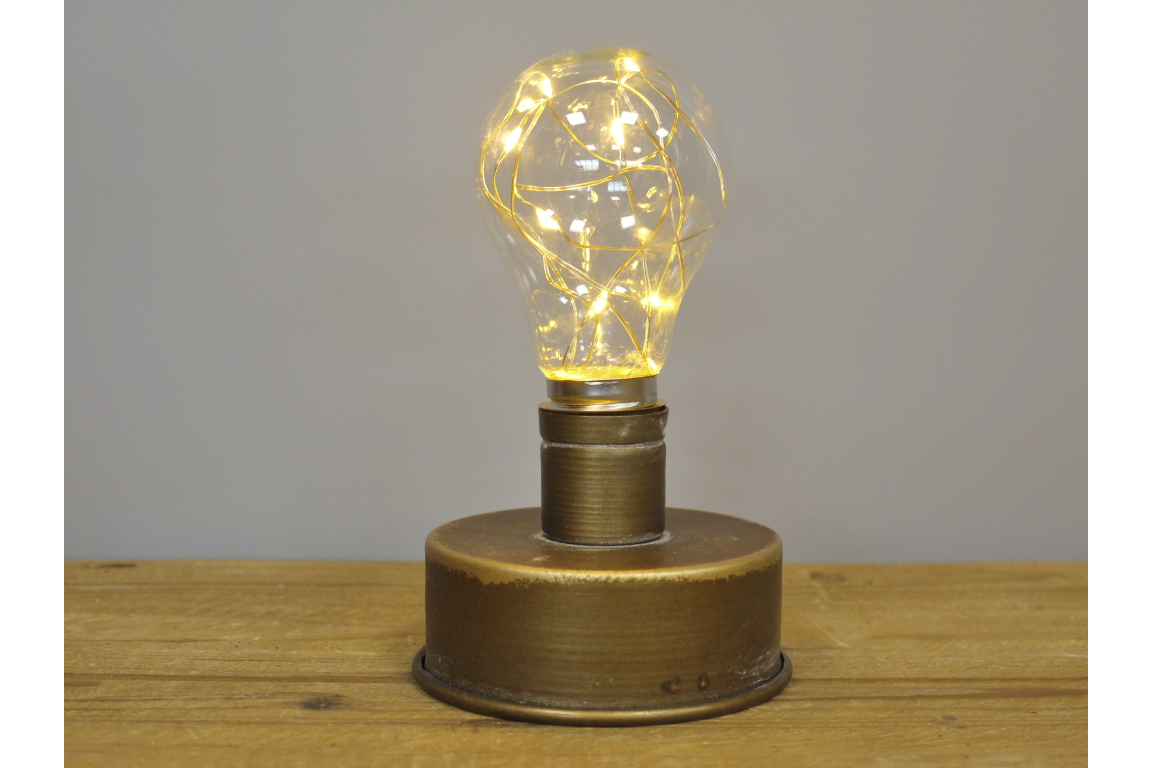 Industrial light with a round bronze metal base and a clear bulb containing warm white string lights on a wooden surface.