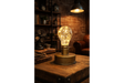 Table lamp with clear glass bulb filled with fairy lights on a round metal base, placed on a wooden table.