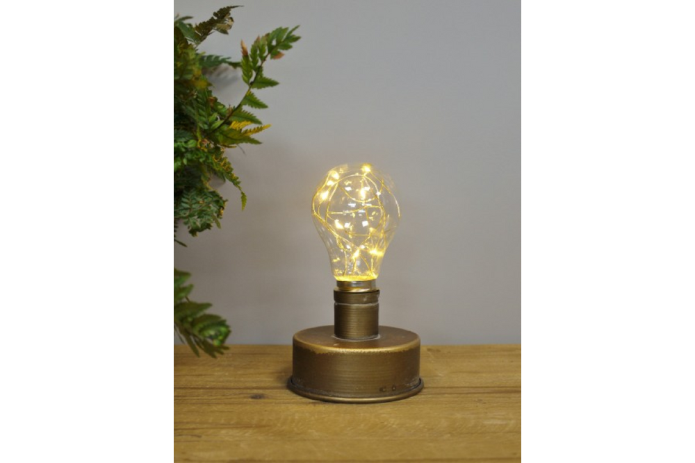 Small bronze industrial table lamp with clear bulb and warm fairy lights on wooden surface, gray background