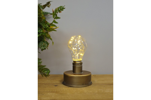 Small bronze industrial table lamp with clear bulb and warm fairy lights on wooden surface, gray background