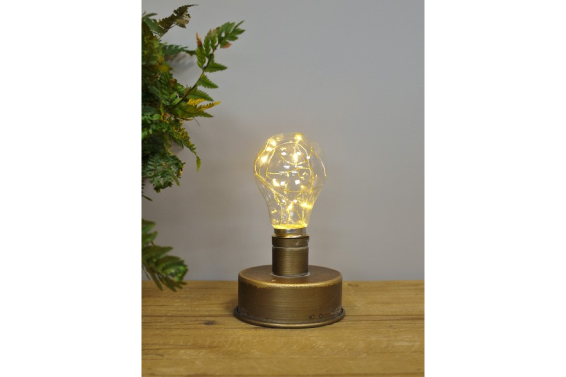 Small bronze industrial table lamp with clear bulb and warm fairy lights on wooden surface, gray background