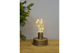 Small bronze industrial table lamp with clear bulb and warm fairy lights on wooden surface, gray background