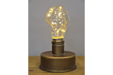 Metallic industrial-style table lamp with a round base and a light bulb filled with warm fairy lights, front view.