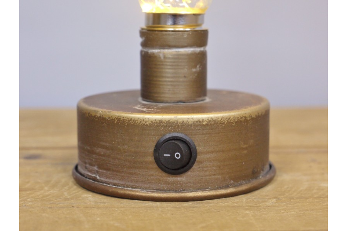 Close-up of round bronze metal base of industrial light with a black on/off switch on wooden surface.