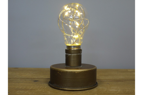 Small industrial-style light with round bronze metal base and bulb-shaped glass cover with warm LED string lights.