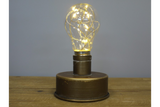 Small industrial-style light with round bronze metal base and bulb-shaped glass cover with warm LED string lights.