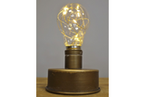 Small industrial-style table light with cylindrical bronze metal base and clear glass bulb with warm LED string lights