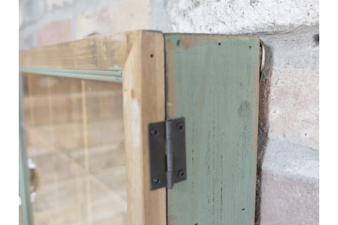 Close-up of rustic wooden cabinet hinge, green painted side next to exposed brick wall