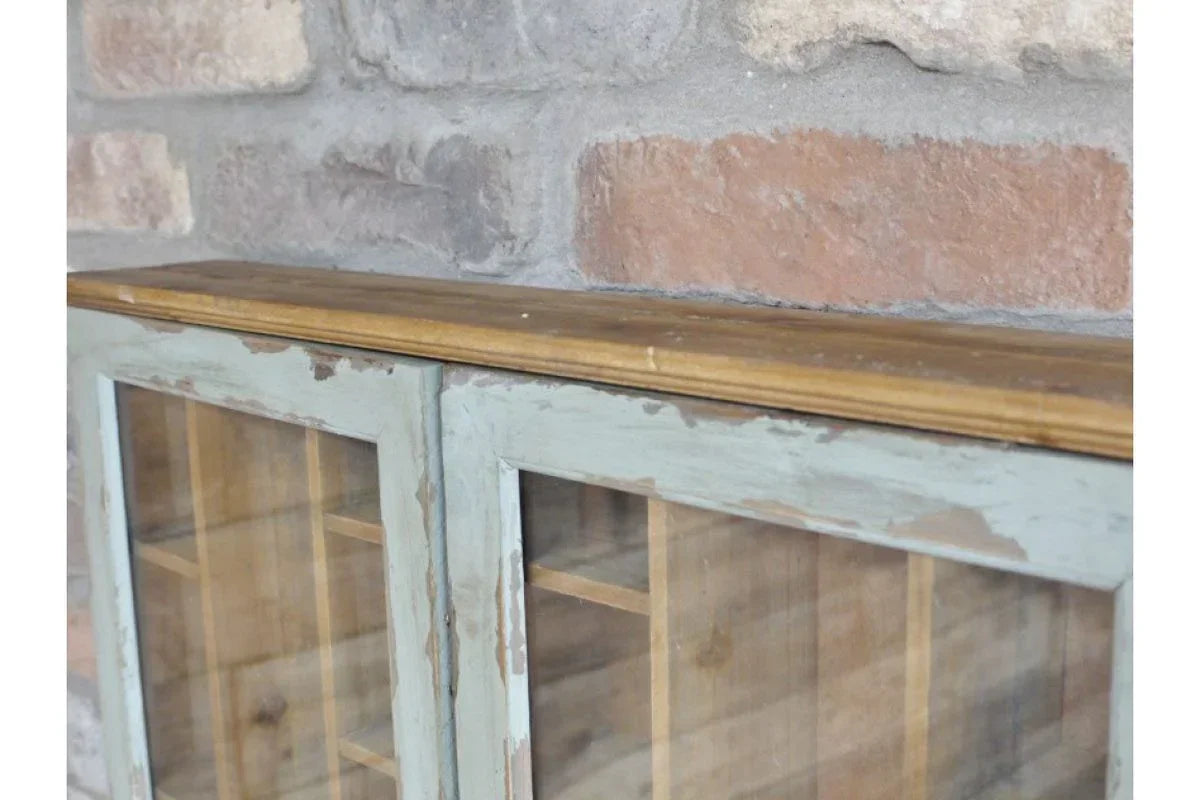 Closeup of rustic wooden cabinet top with distressed paint and glass doors against brick wall