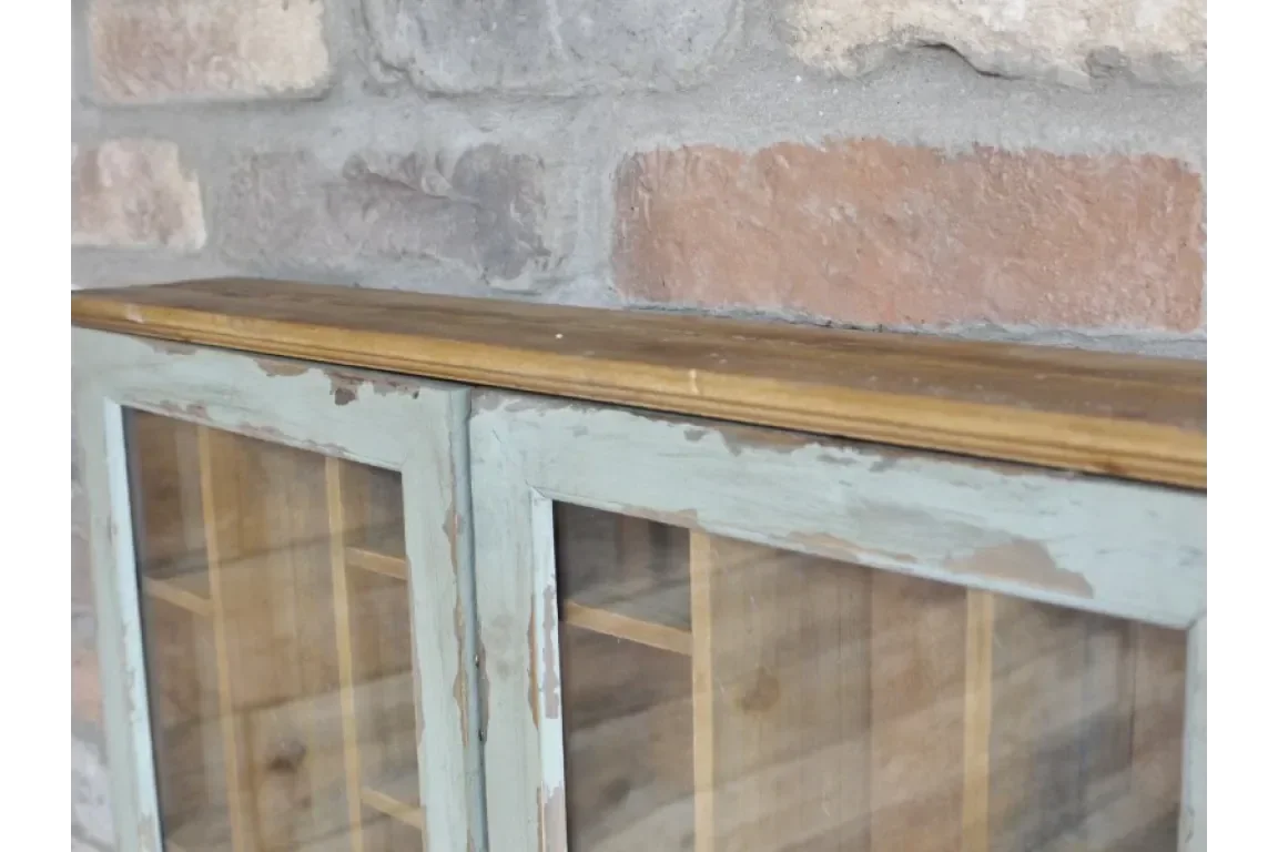 Distressed wood display cabinet with glass doors against a brick wall