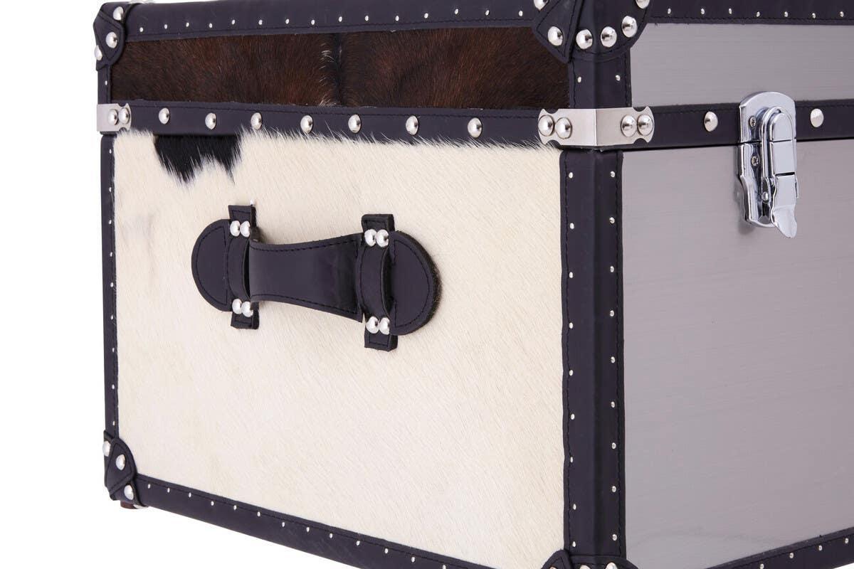 Cowhide trunk with black leather trim, metal studs, and chrome latch, close-up view