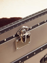 A close-up view of a black and white hair-on-leather cabinet featuring three drawers. The cabinet has a sleek metallic latch and decorative metal accents along the edges, showcasing a stylish and modern design. The texture of the leather is visible, highlighting its unique pattern