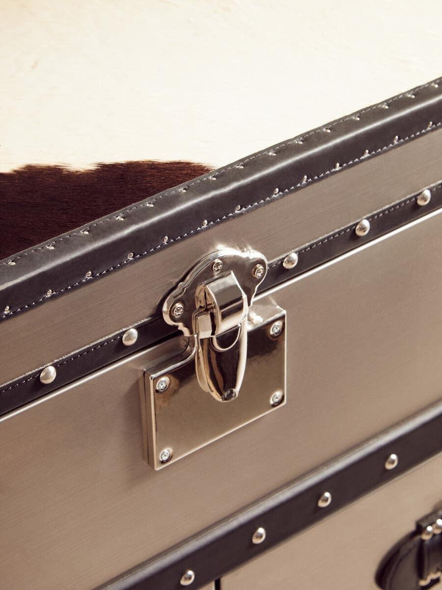 A close-up view of a black and white hair-on-leather cabinet featuring three drawers. The cabinet has a sleek metallic latch and decorative metal accents along the edges, showcasing a stylish and modern design. The texture of the leather is visible, highlighting its unique pattern