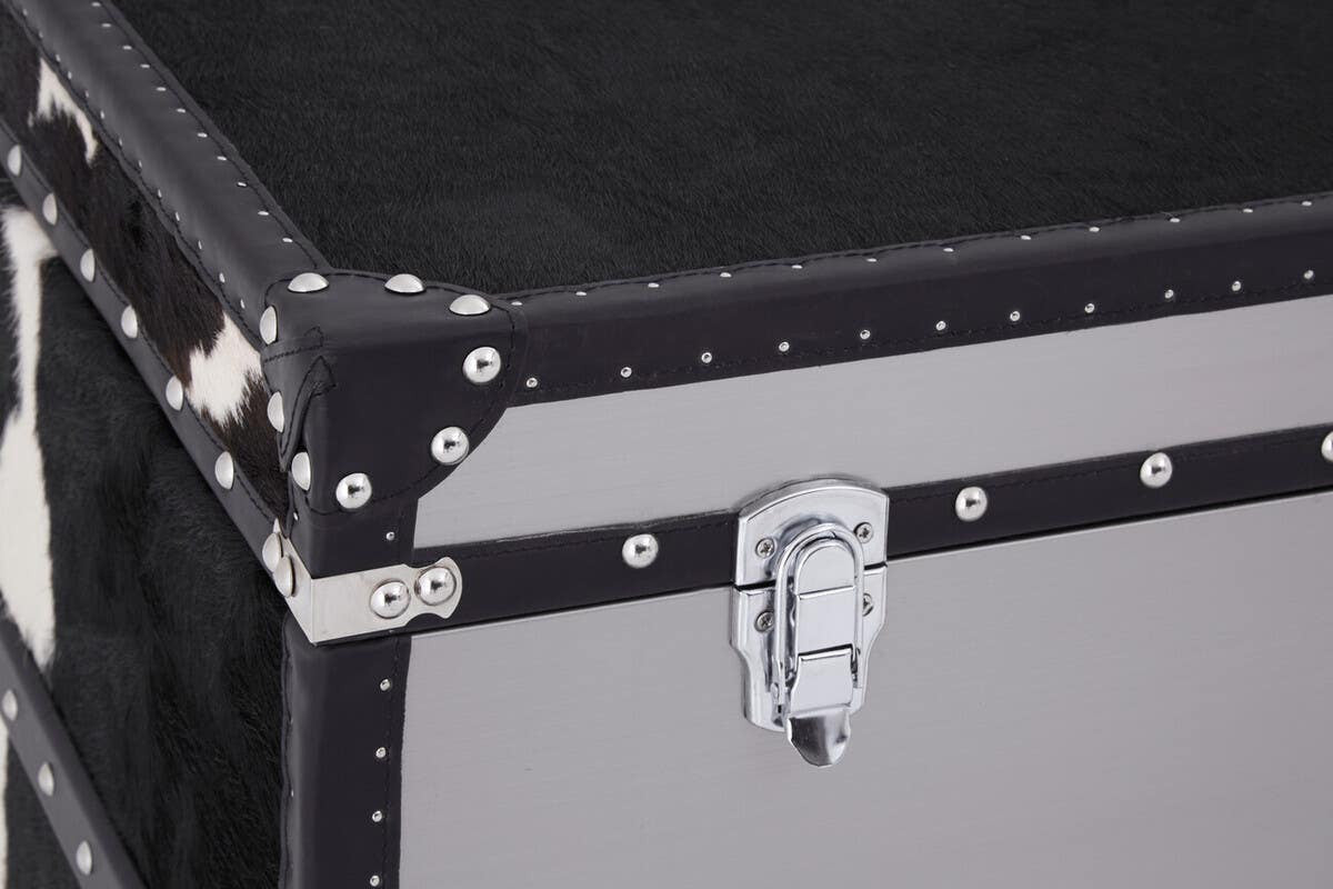 Black and white hair-on-leather cabinet featuring three drawers, with a sleek design and metal accents. The corners are reinforced with silver studs, and a sturdy latch is visible on the front. The surface has a smooth finish, highlighting the contrasting textures of the leather