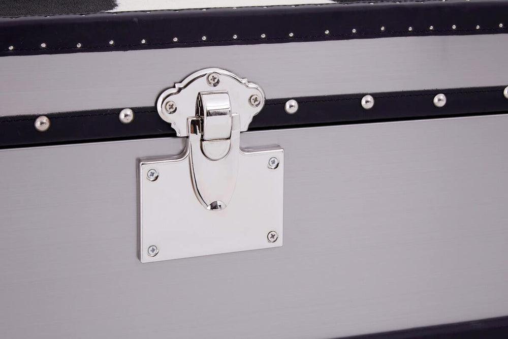 A close-up view of a black and white hair-on-leather cabinet featuring three drawers. The cabinet has a sleek design with a metal latch and a decorative white plate. The texture of the hair-on-leather is visible, showcasing a mix of black and white patterns