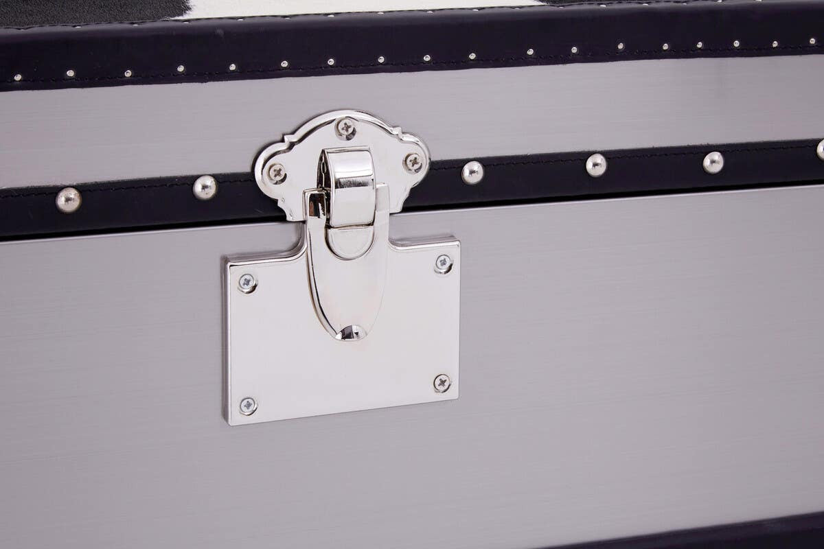 A close-up view of a black and white hair-on-leather cabinet featuring three drawers. The cabinet has a sleek design with a metal latch and a decorative white plate. The texture of the hair-on-leather is visible, showcasing a mix of black and white patterns