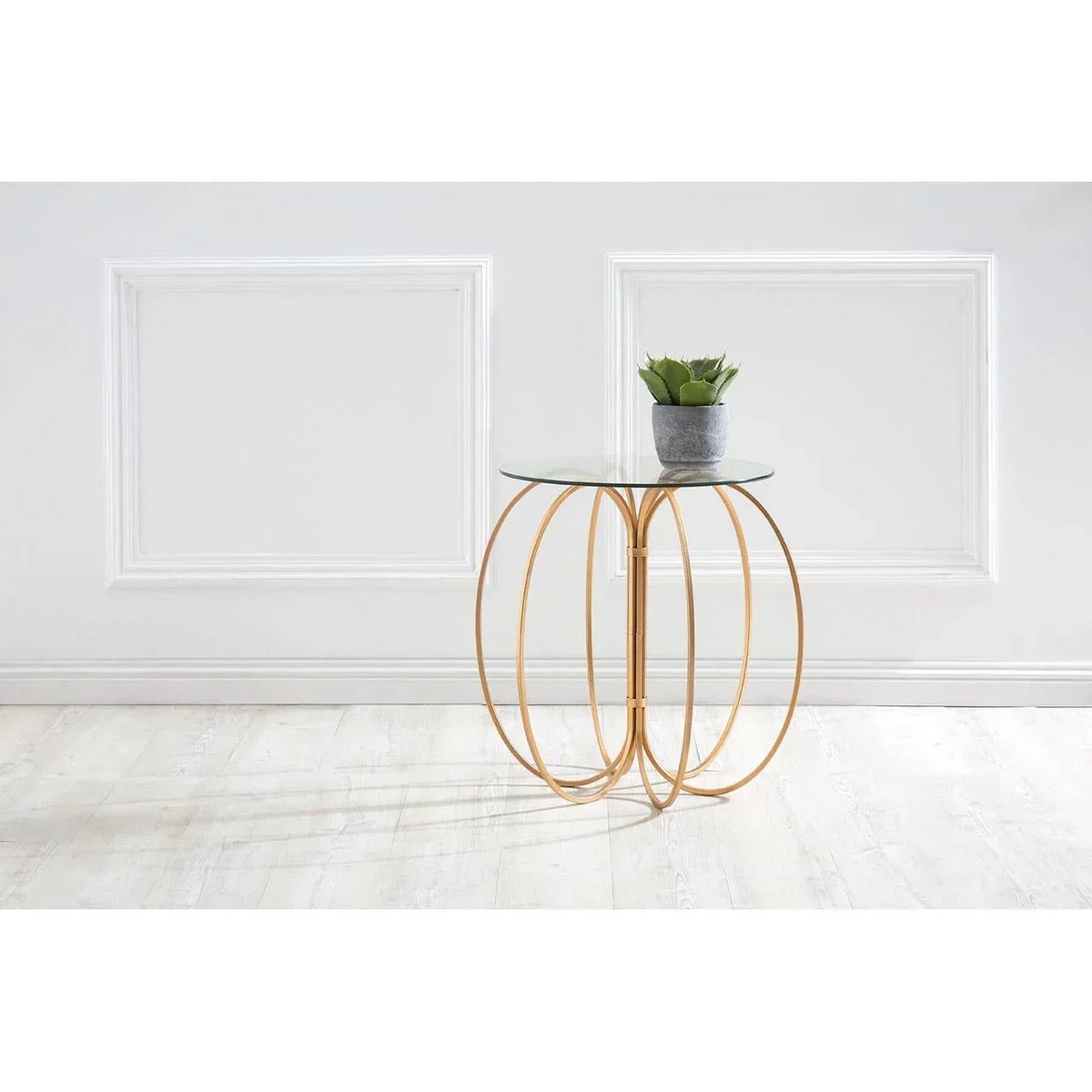 Glass top side table with gold metal frame and potted plant, set against a white wall