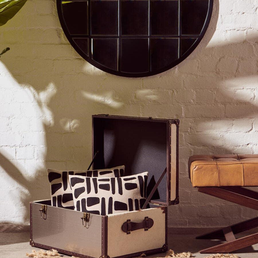 Storage trunk with black trim open, holding two patterned cushions beside tan bench