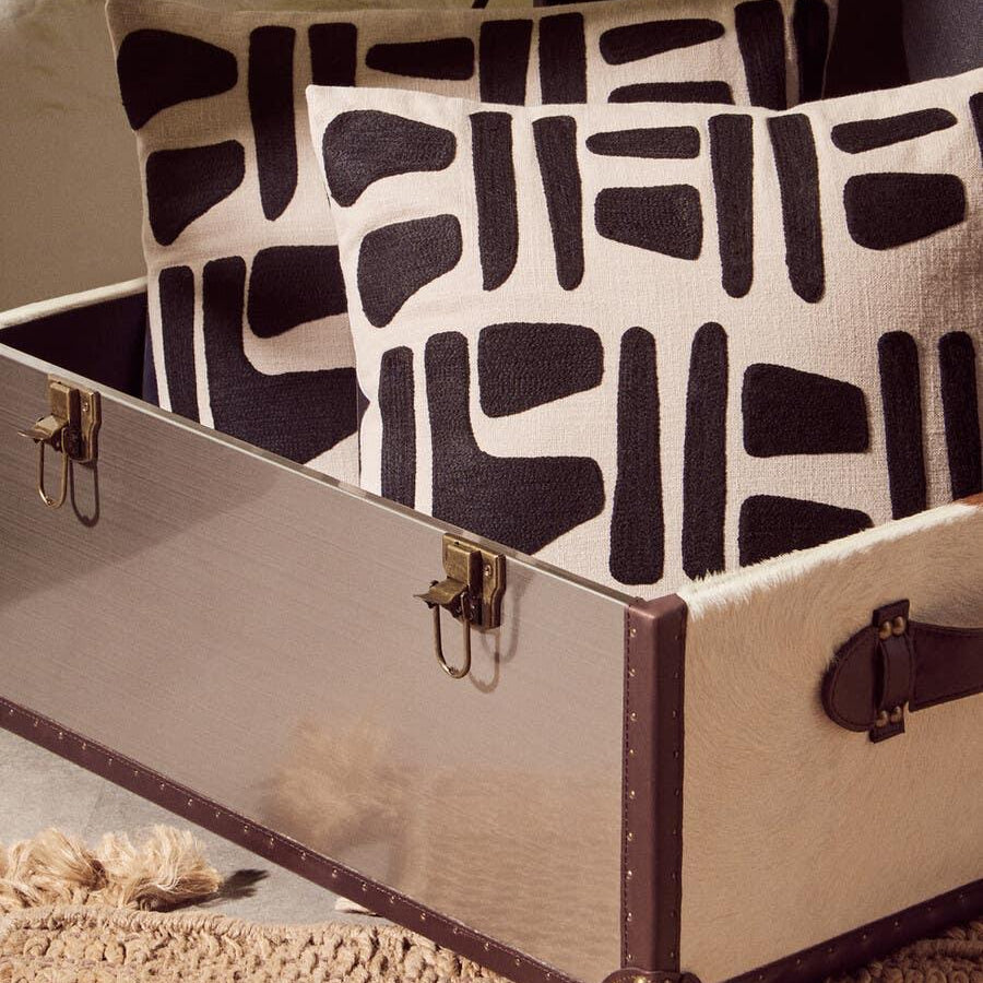 Geometric black and cream cushions placed inside a decorative storage trunk on woven rug