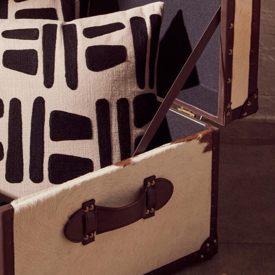 Two patterned black and cream cushions in a cowhide storage trunk on a textured rug