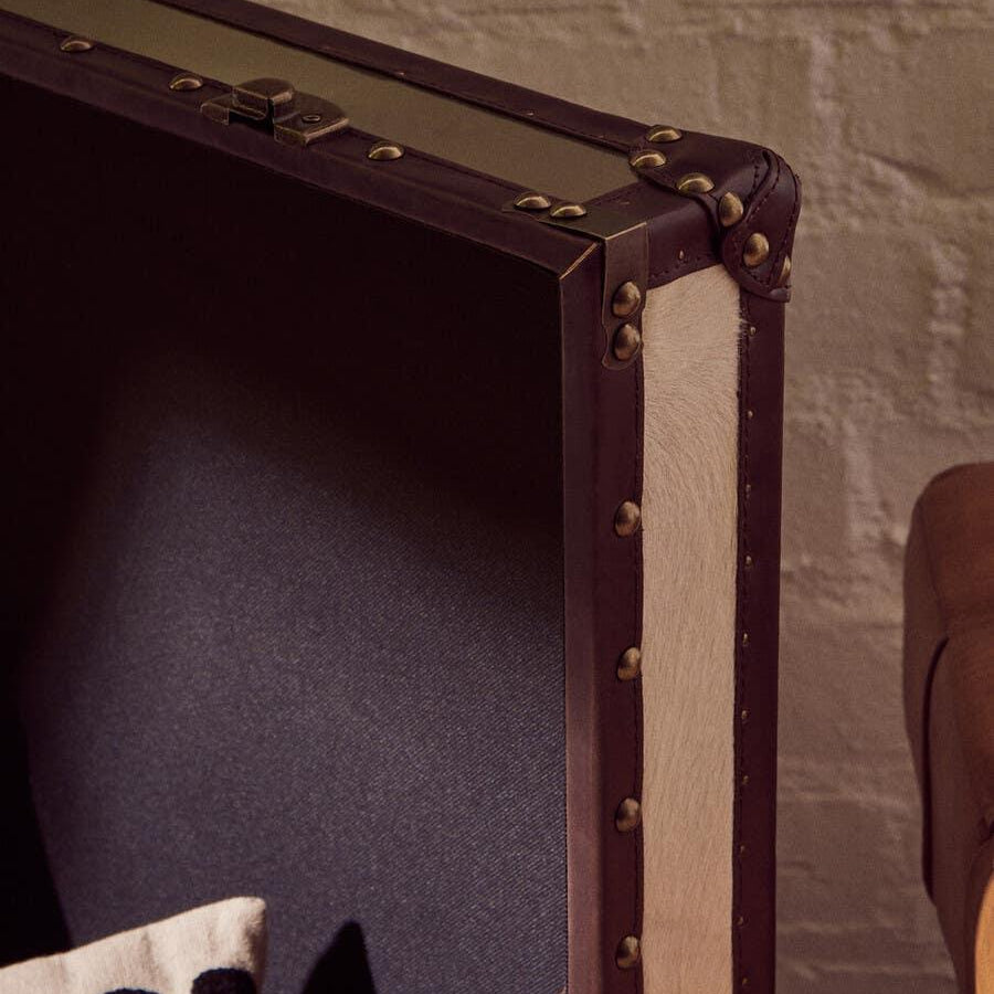 Close-up of leather-trimmed storage trunk with metal rivets and fabric cushion