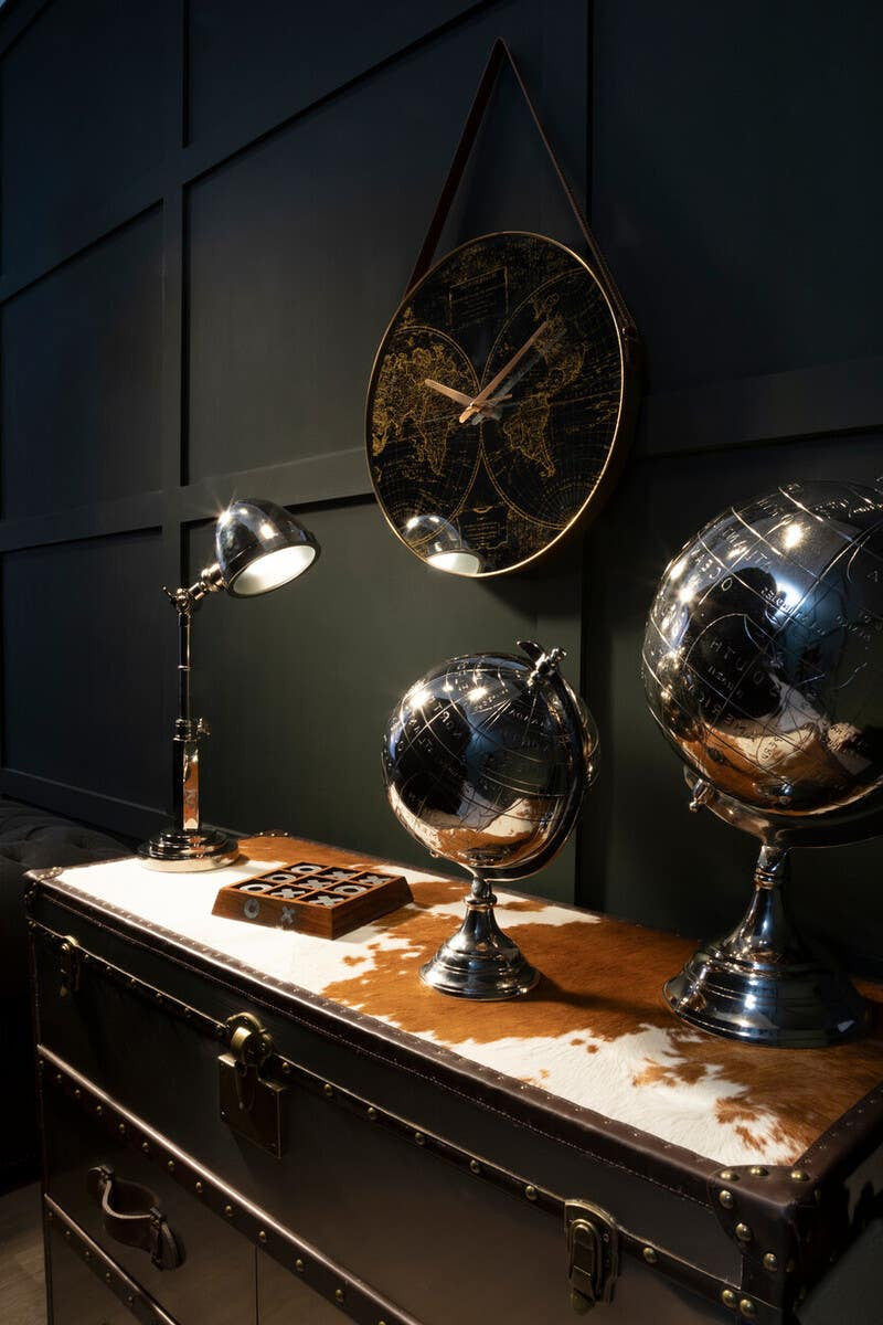 A stylish brown and white cowhide cabinet with a wooden top, placed against a dark wall. On the cabinet, there are two decorative globes, a vintage-style lamp, and a leather-bound book, creating an elegant and sophisticated atmosphere