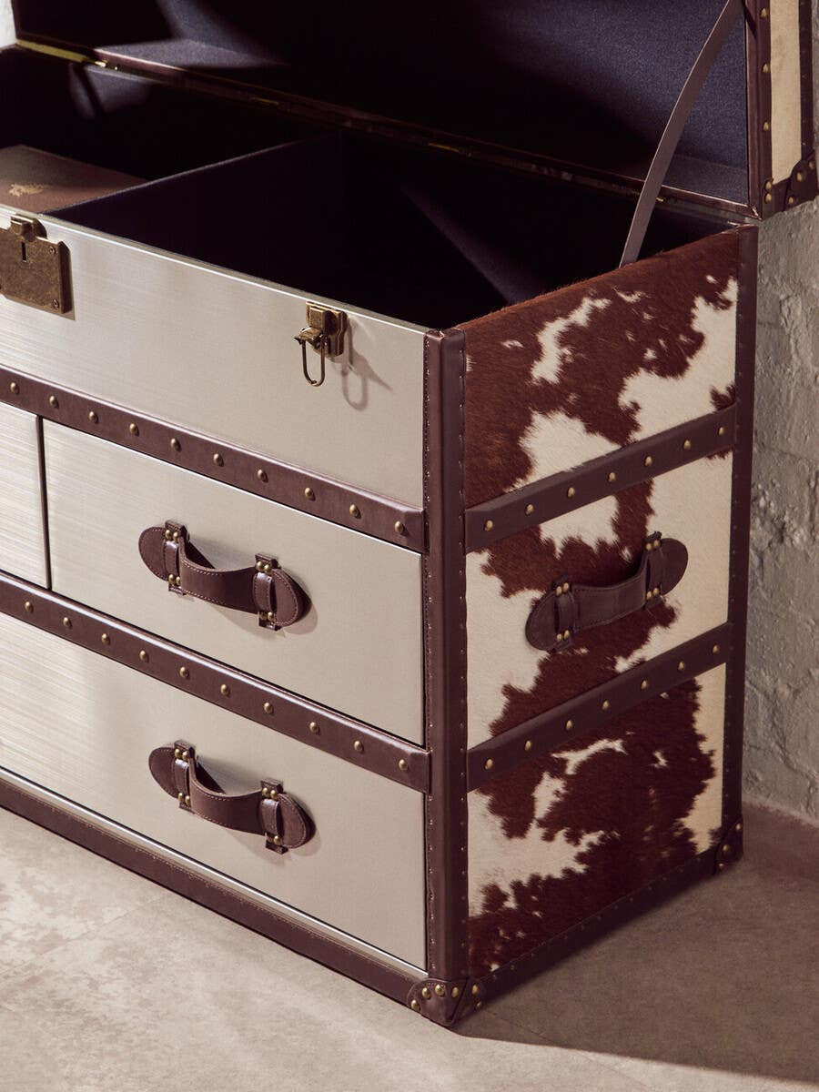 Brown and white cowhide cabinet featuring two drawers with decorative handles, showcasing a mix of smooth and textured surfaces. The cabinet has a rich brown base with a unique cowhide pattern, and the interior is open, revealing storage space. The cabinet is placed on a light-colored wooden floor