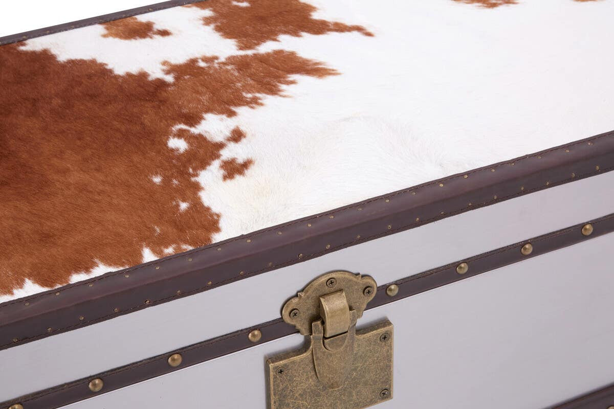 A close-up view of the Kensington Townhouse cabinet featuring a brown and white cowhide top with a natural pattern, complemented by a sleek white base and a decorative gold latch