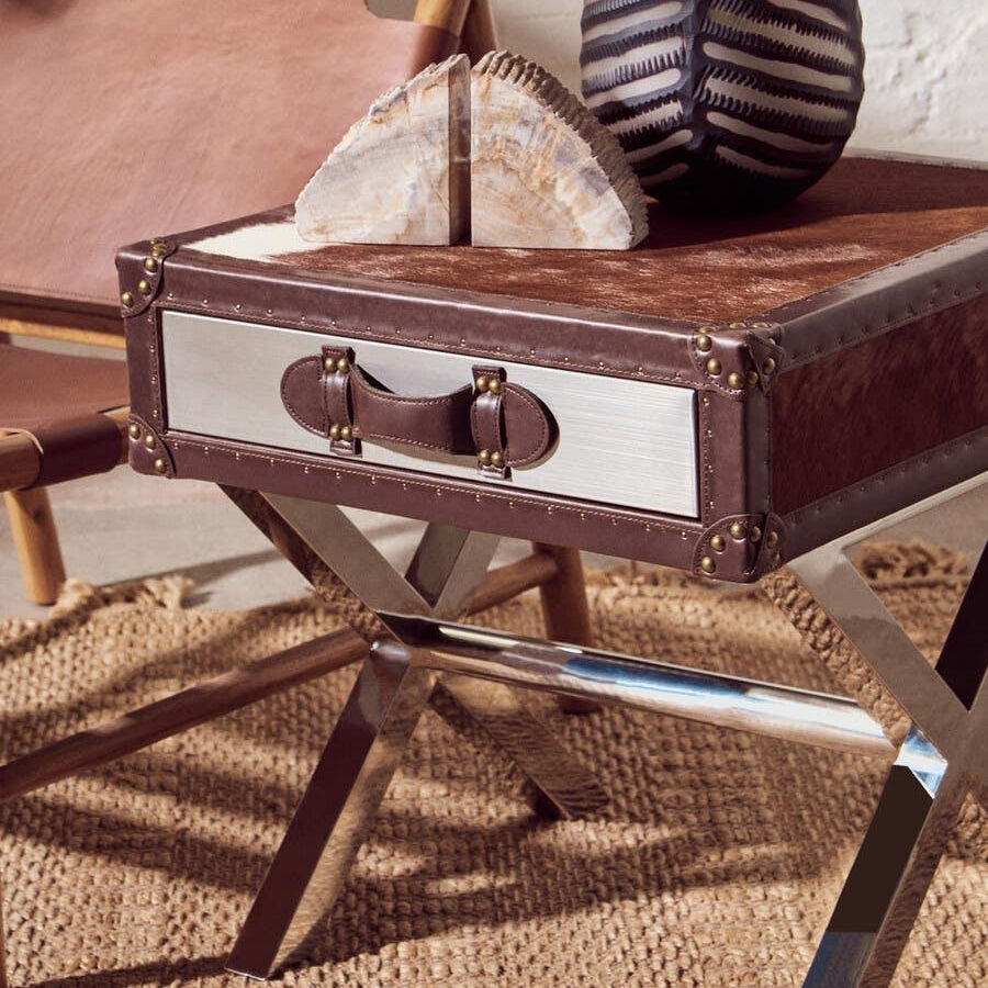 Brown leather side table with chrome legs, woven rug, and ceramic vase with plant