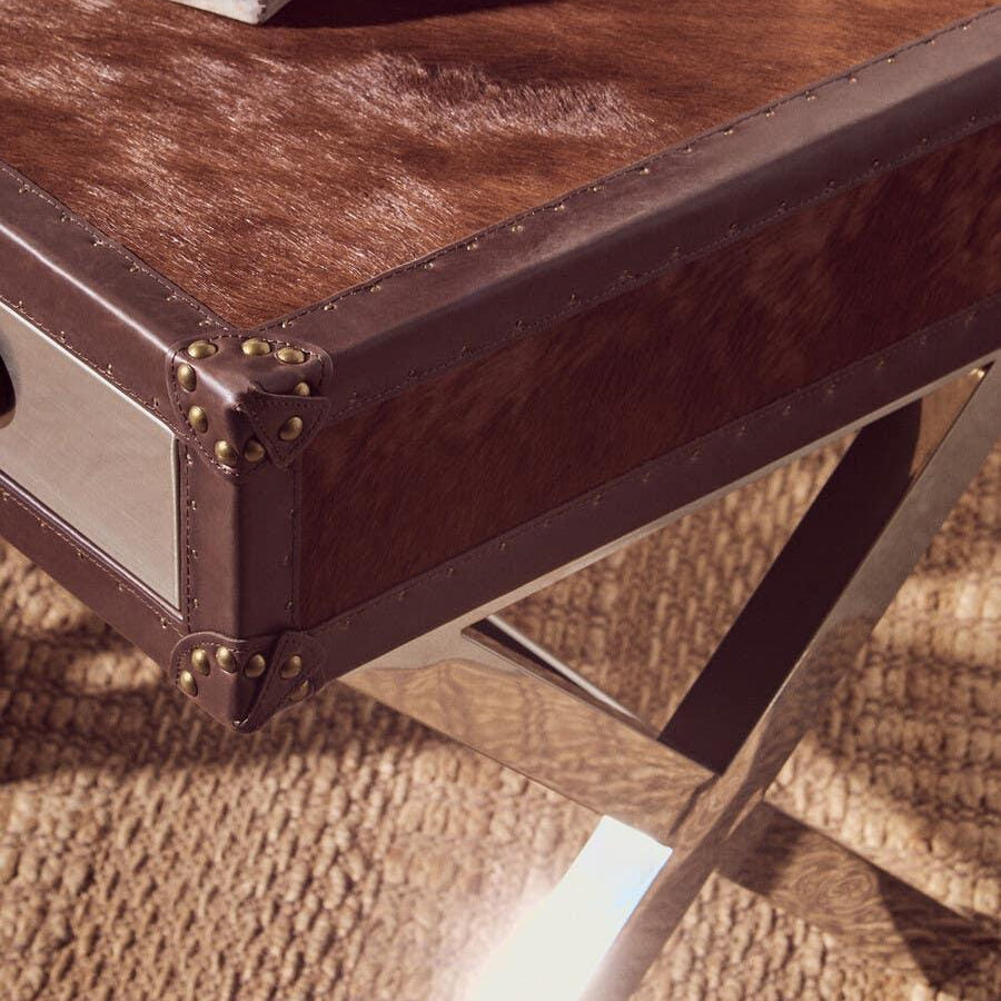 Brown leather coffee table with metal corners and crossed metal legs on woven rug