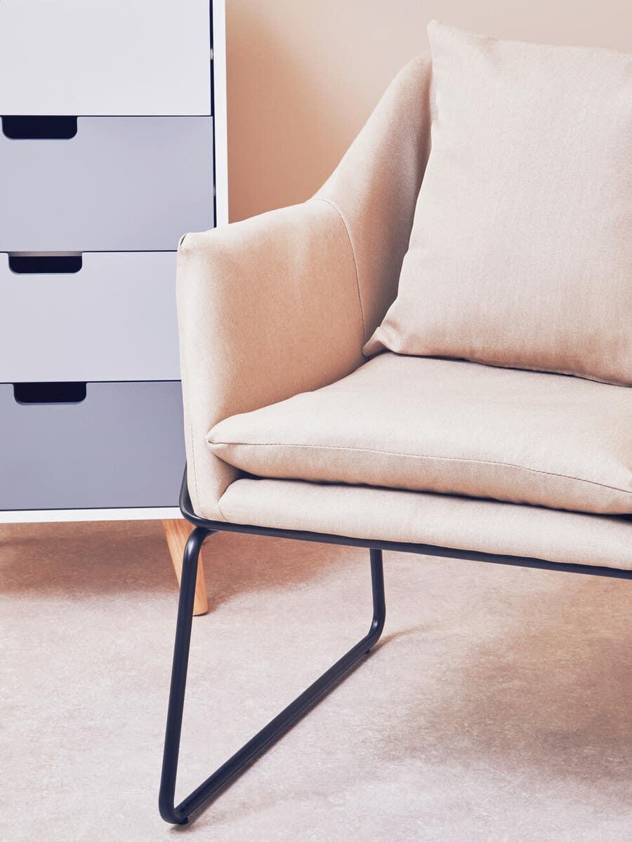 Beige upholstered armchair with metal legs next to grey and white storage drawers