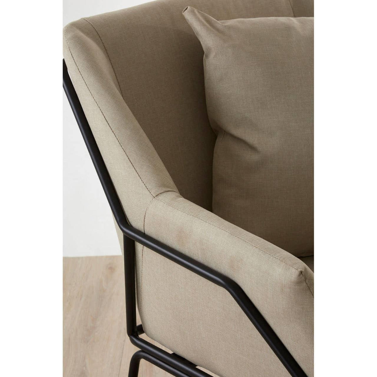 Beige fabric armchair with black metal frame and matching cushion, angled close-up view