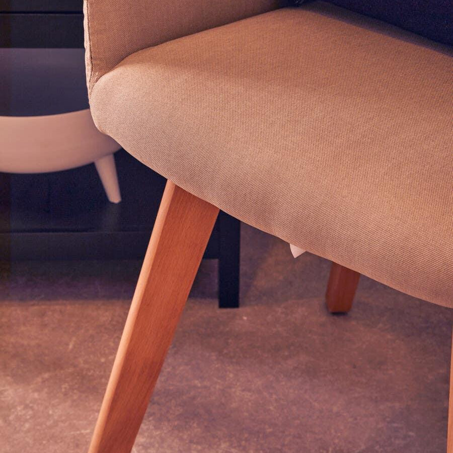 Beige upholstered dining chair with wooden legs closeup on textured floor