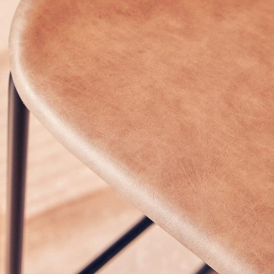 Light brown faux leather bar stool seat with black metal legs close-up