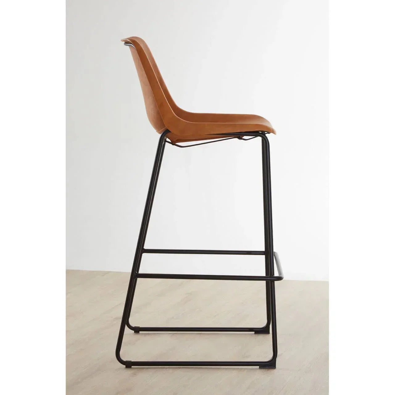 Brown bar stool with curved seat and black metal frame on light wood floor, side view