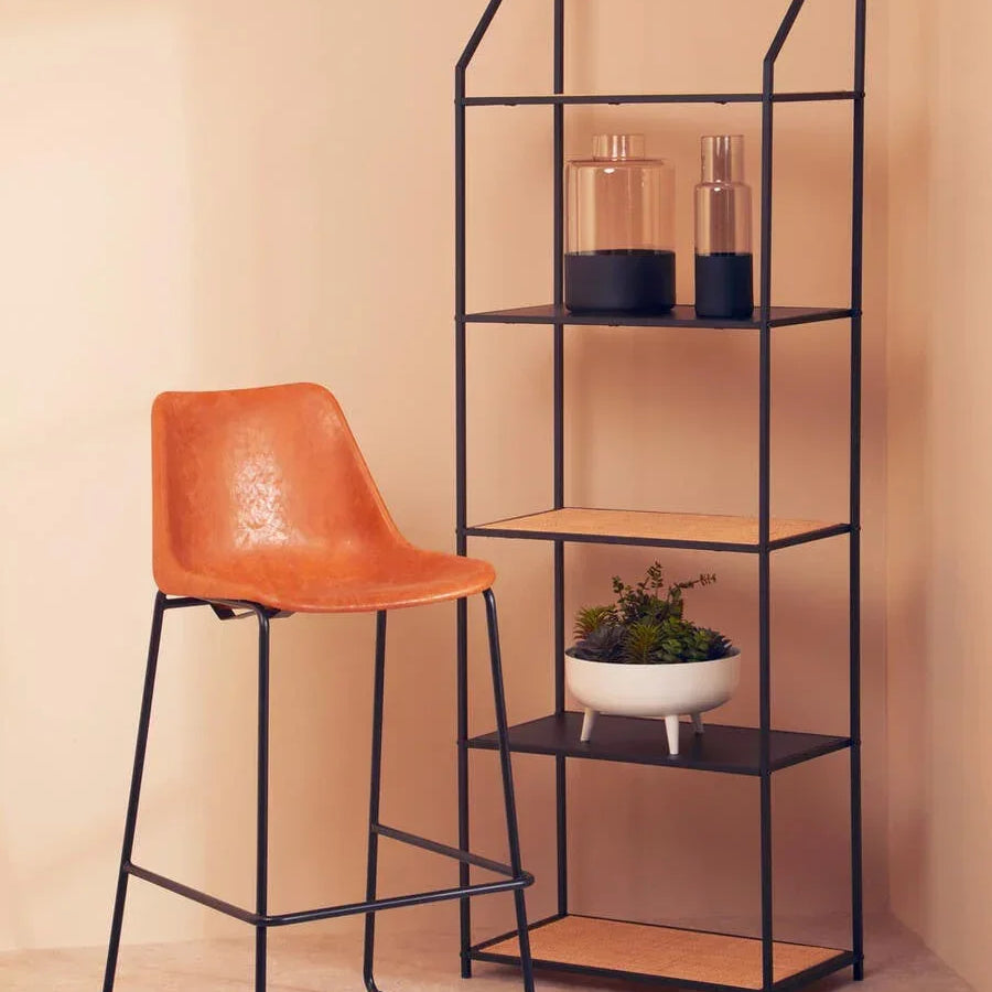 Brown faux leather bar stool with black metal legs beside black metal shelving unit