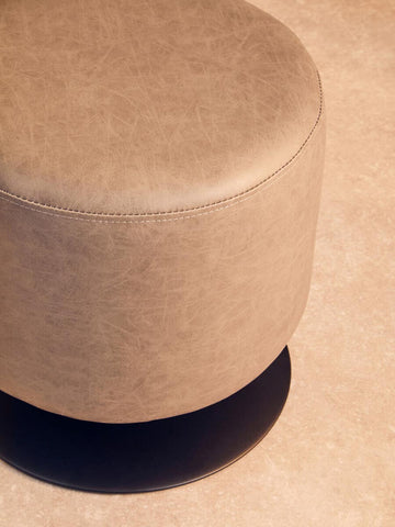 Round pouffe in ash grey faux leather with a smooth surface and a subtle sheen, casting a soft shadow on a light-colored floor