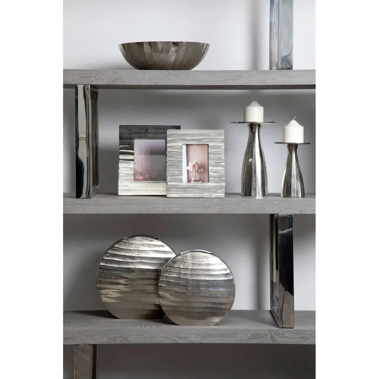 Silver metal decorative photo frames, candle holders and bowls on wooden shelving unit